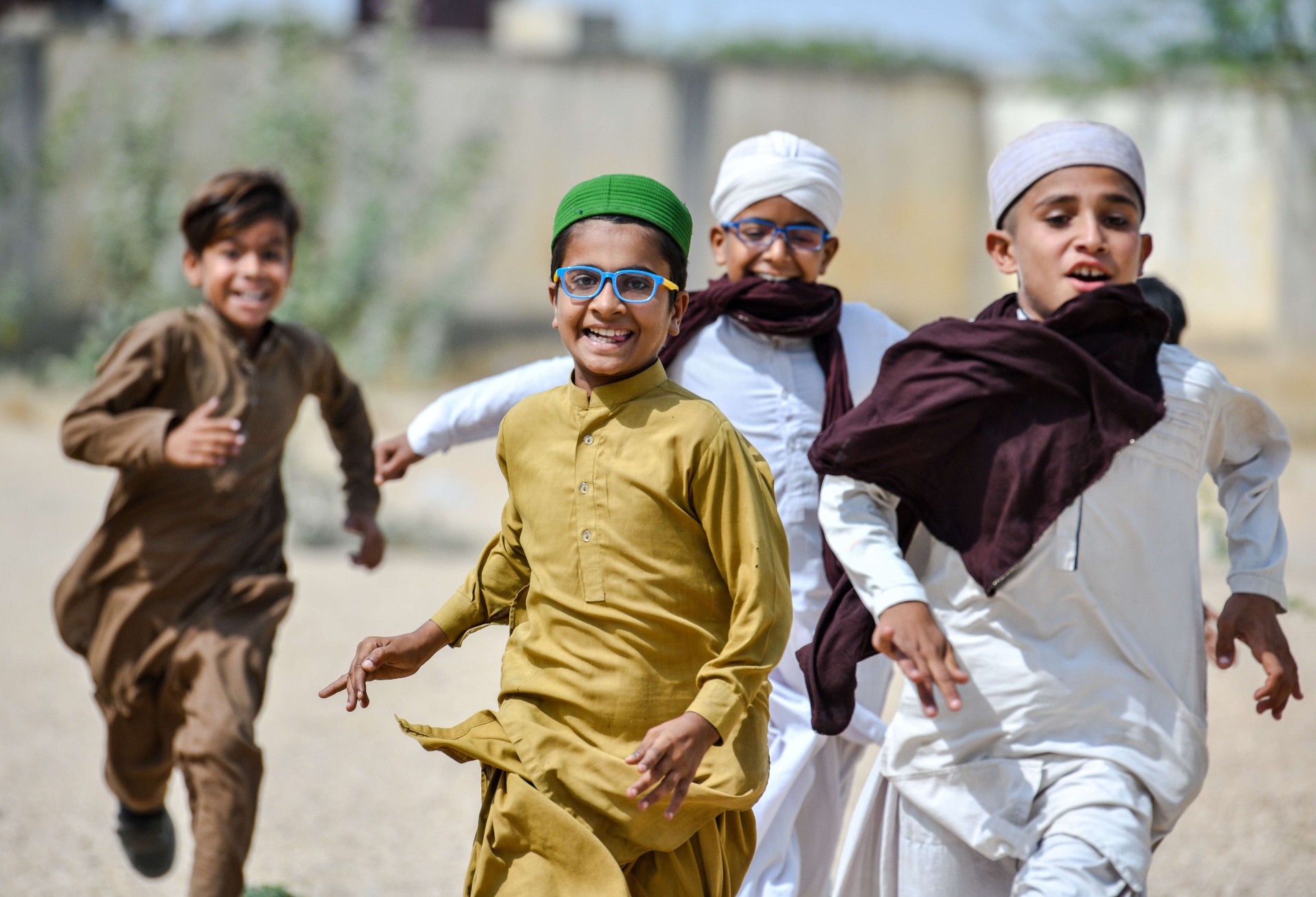 Close-up of four Pakistani boys mid-run, two wearing their new prescription glasses