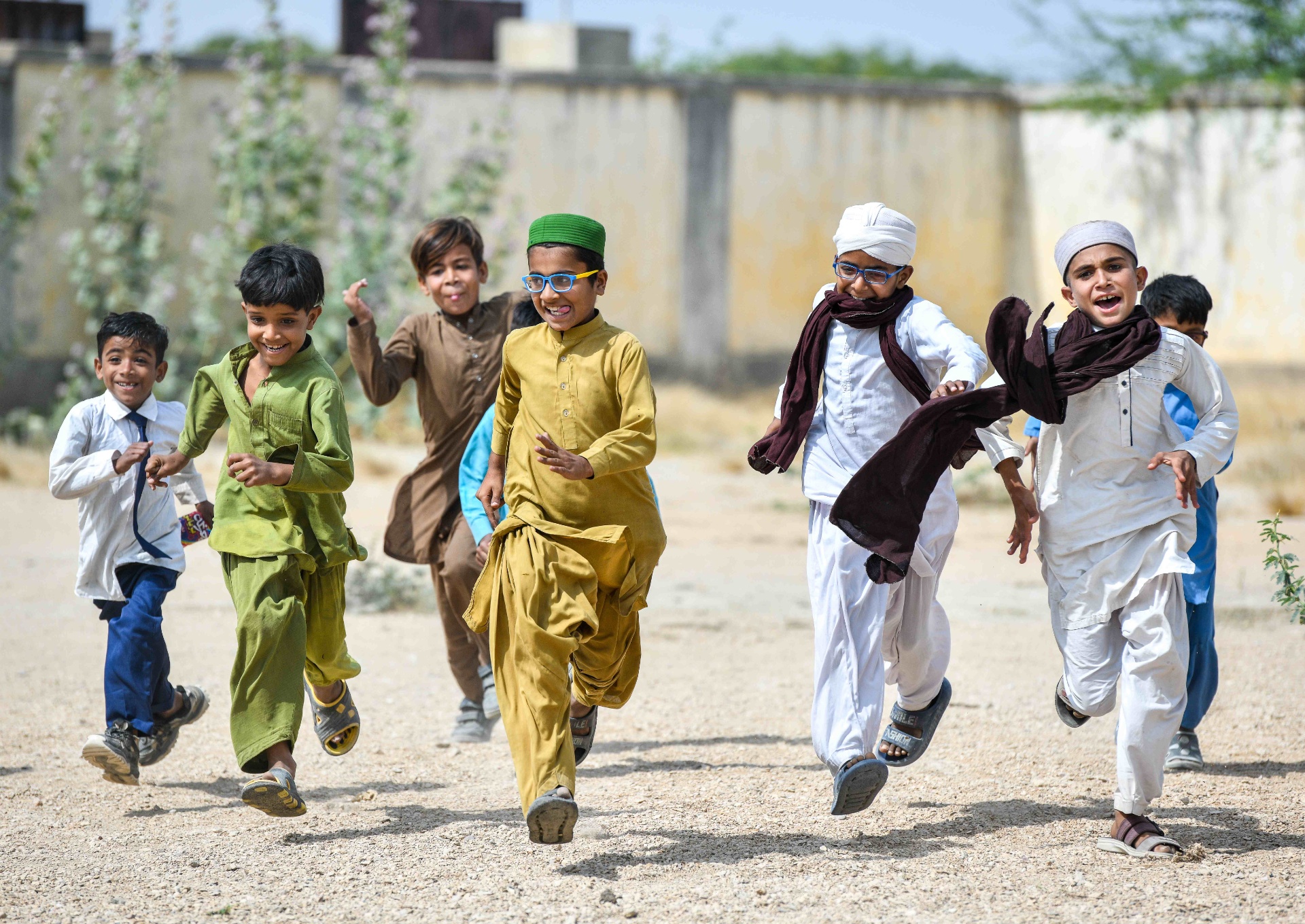 Pakistani boy in yellow kurta and blue OSaaT glasses leads friends in a joyful run
