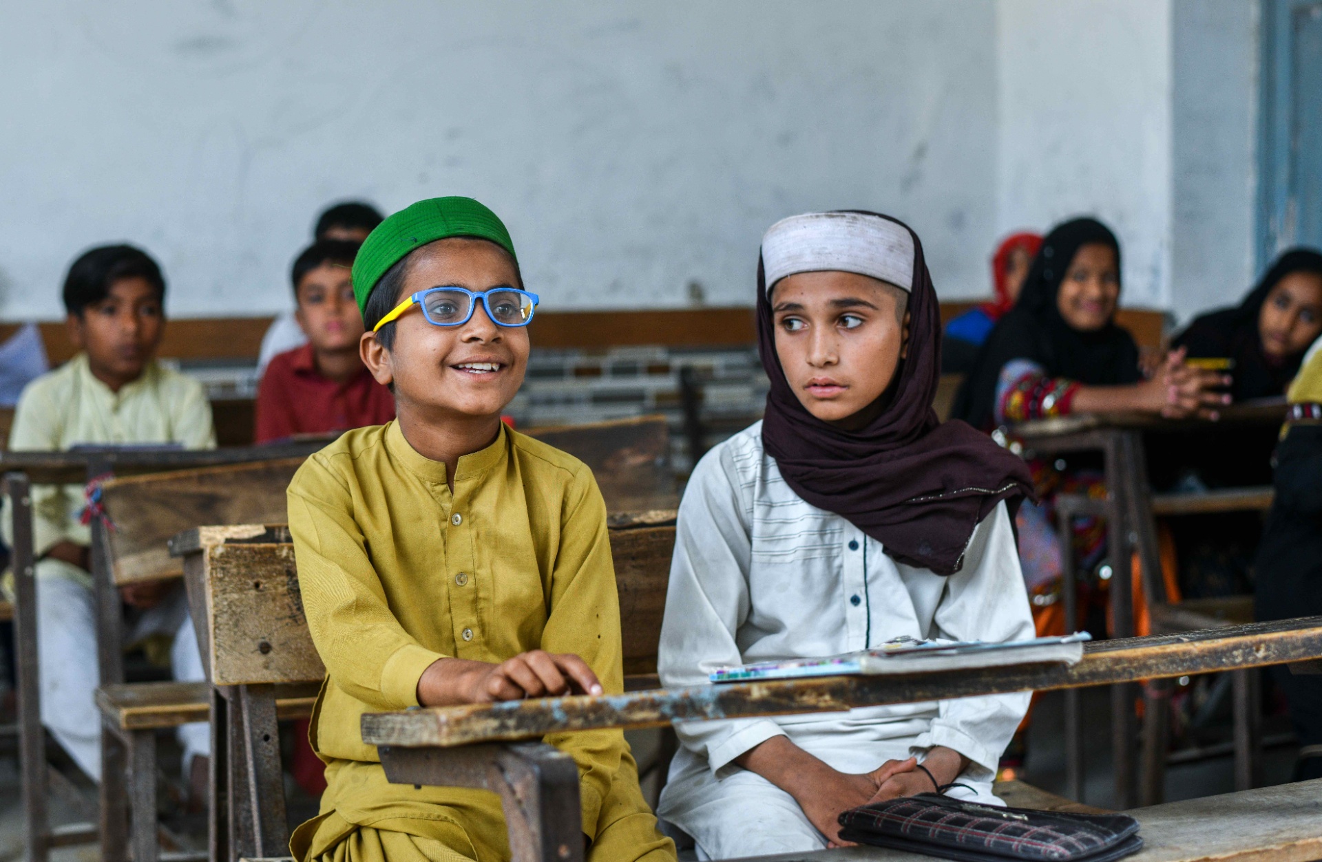 Two Pakistani students share a classroom desk, one wearing his new OSaaT glasses