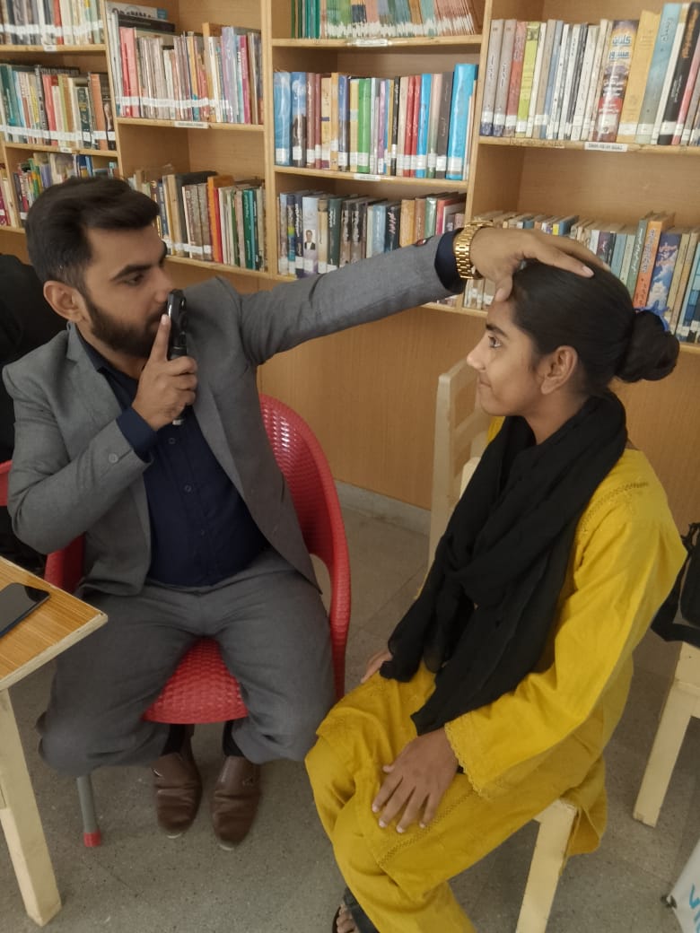 Optometrist examines a student with a retinoscope in a school library, Pakistan
