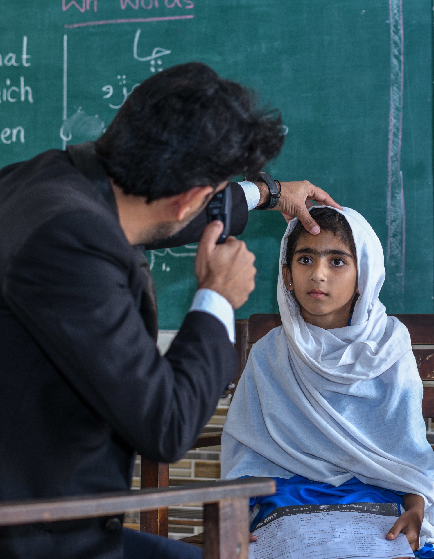 Optometrist performs retinoscopy on a Pakistani schoolgirl using an OSaaT/OneSight/Berkeley Vision/ZMT screening form