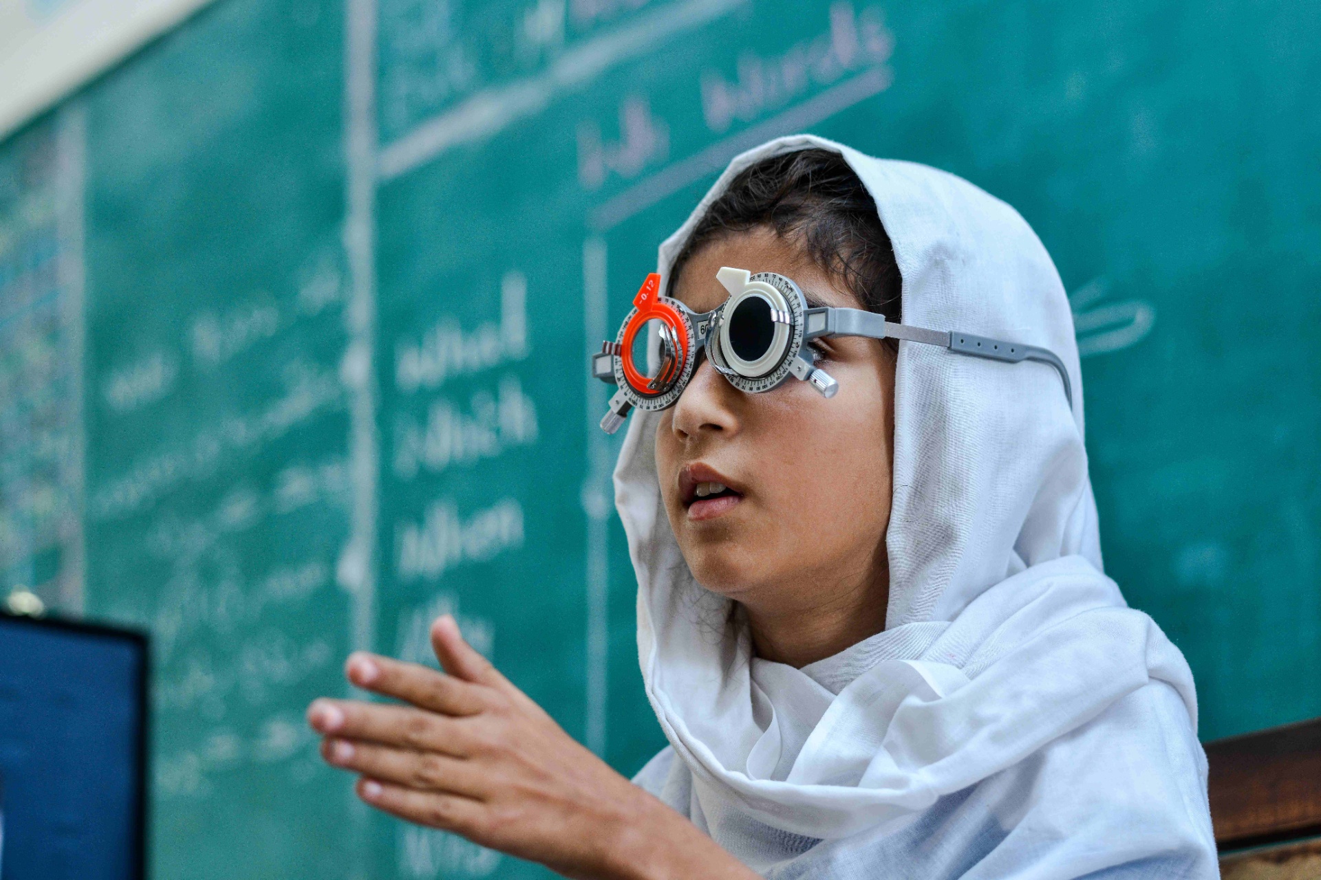 Pakistani schoolgirl wears a trial frame in front of a chalkboard during refraction