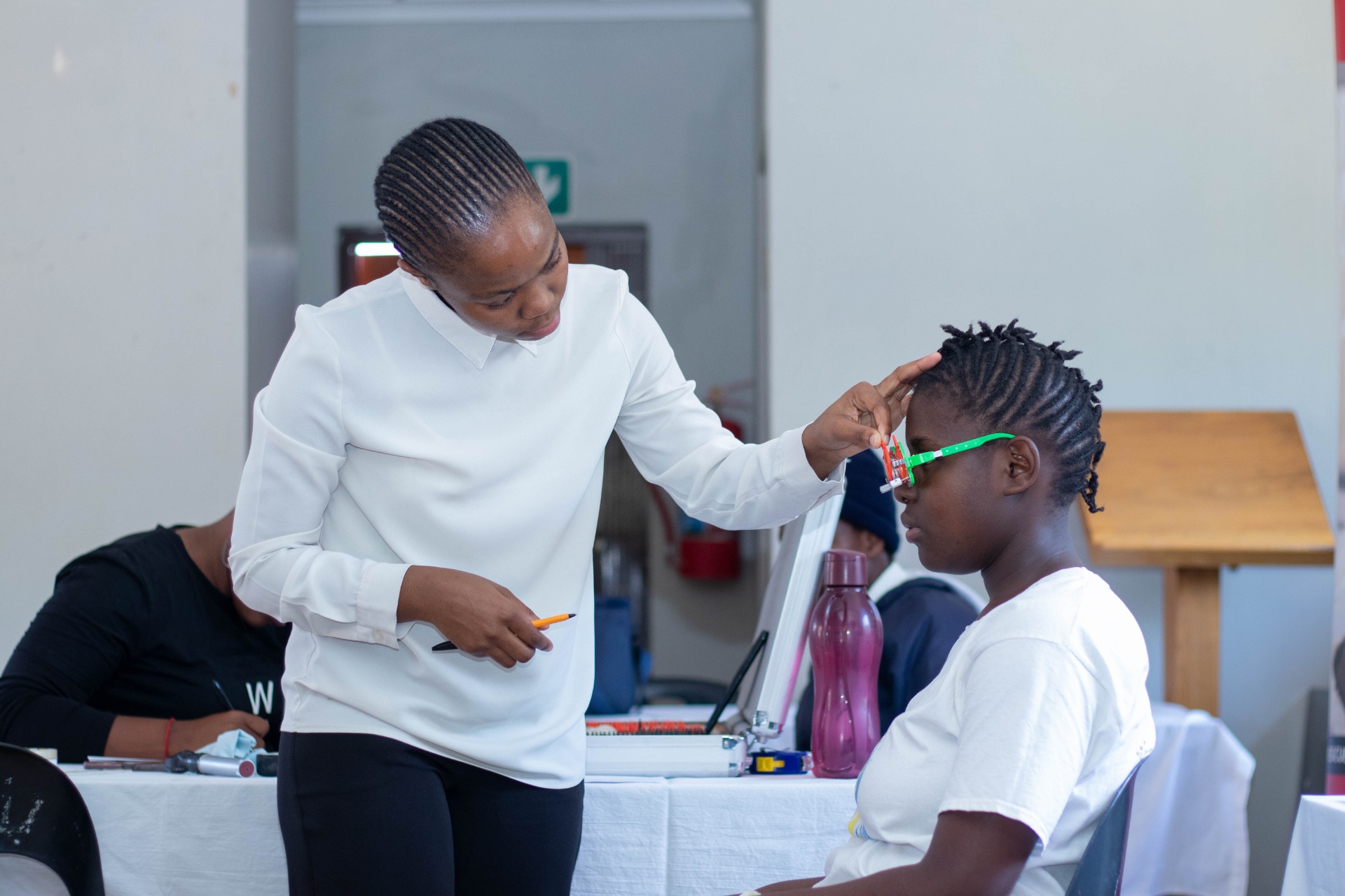 Optometrist adjusts trial frame on student during refraction in South Africa